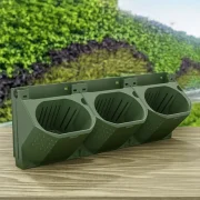 Three green tri-compartment outdoor waste bins mounted on a backplate, set on a wooden surface with a garden background, for sorting garden waste.